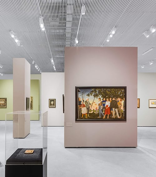 Recessed track light channels fitted with monopoint spotlights and linear surface-mount lights showcase paintings in an art gallery.