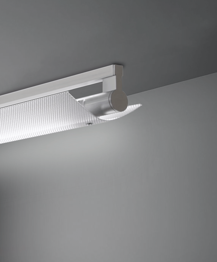 Alcon 12160-PDI-S, surface linear ceiling light shown in silver finish, a tubular half-lit trim-less lens, and a wide curved perforated lens cap.