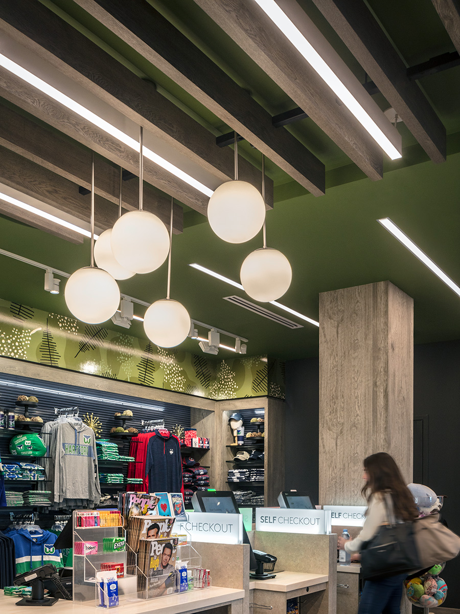 Linear pendant lights hang between wooden ceiling slats, while globe pendants provide task lighting over a checkout counter.