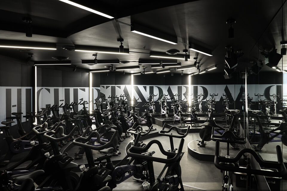Black surface-mount linear lights in a fanned layout on the ceiling and walls of a spin class mimic the light pattern of a hyperspace jump.